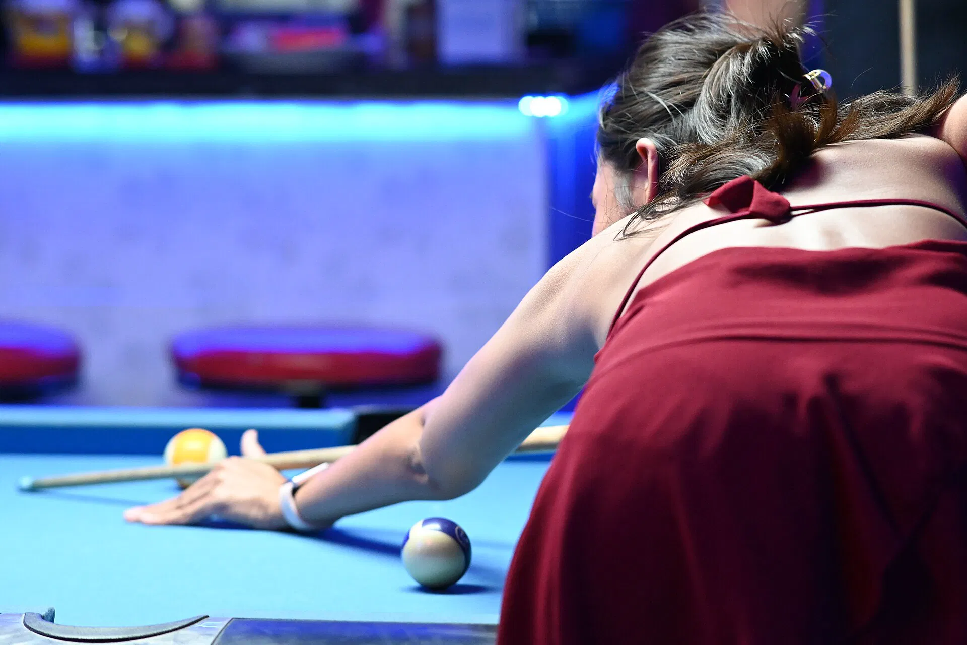 A player leans over a pool table lining up a shot under arena lights