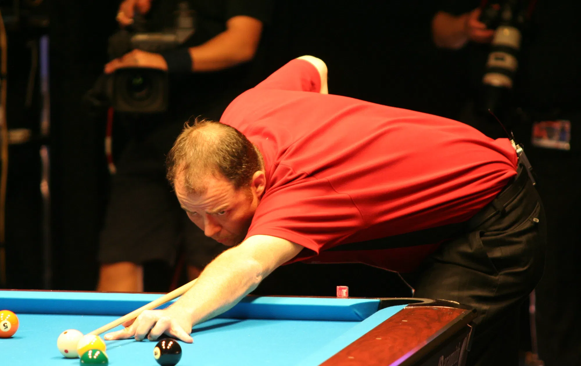 A professional player leans low over the table for a shot under arena lights (Photo: Christian Werner, CC BY 3.0, via Wikimedia Commons)